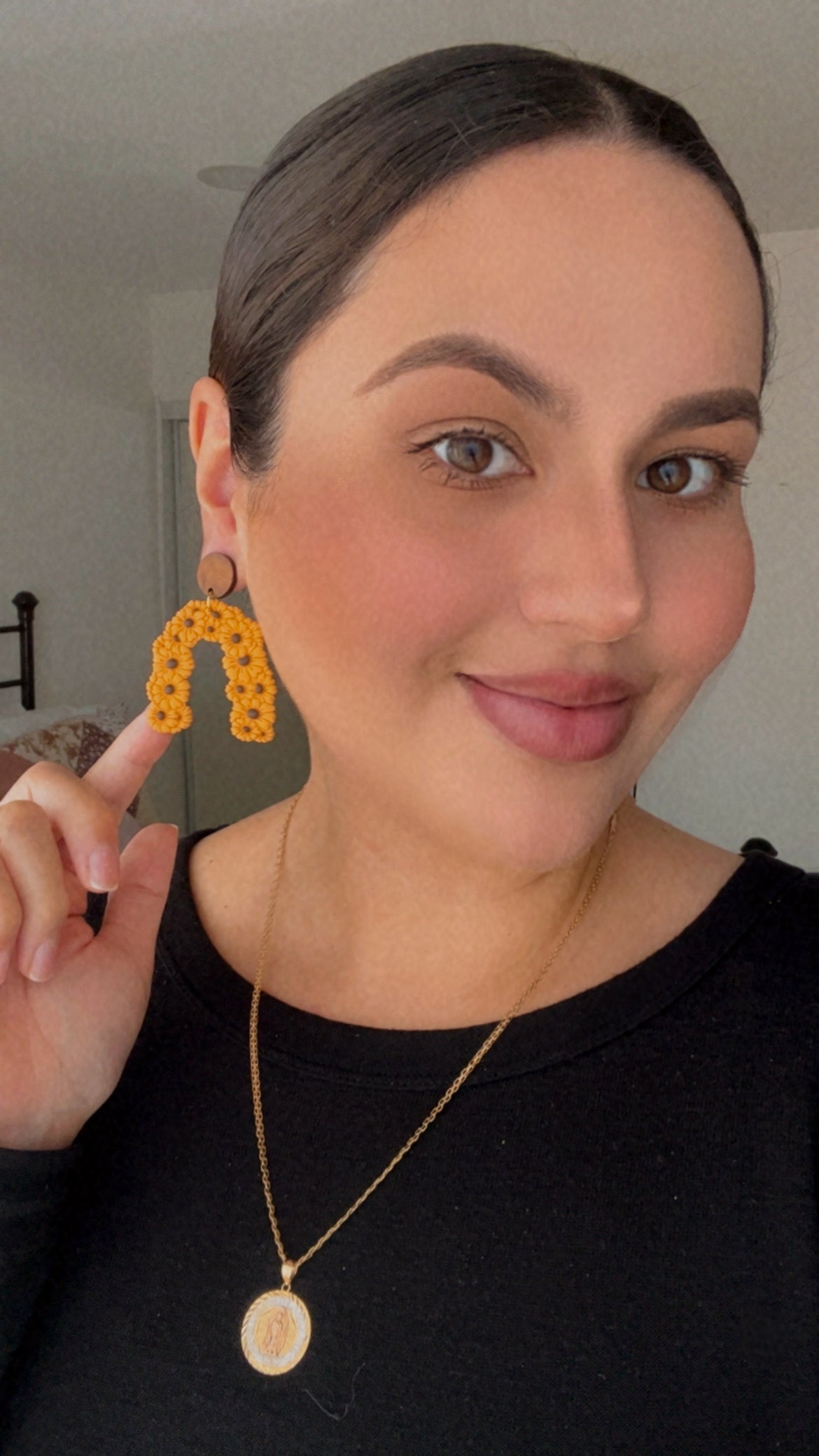 Woman wearing yellow floral earrings and a black top, with a neutral background.