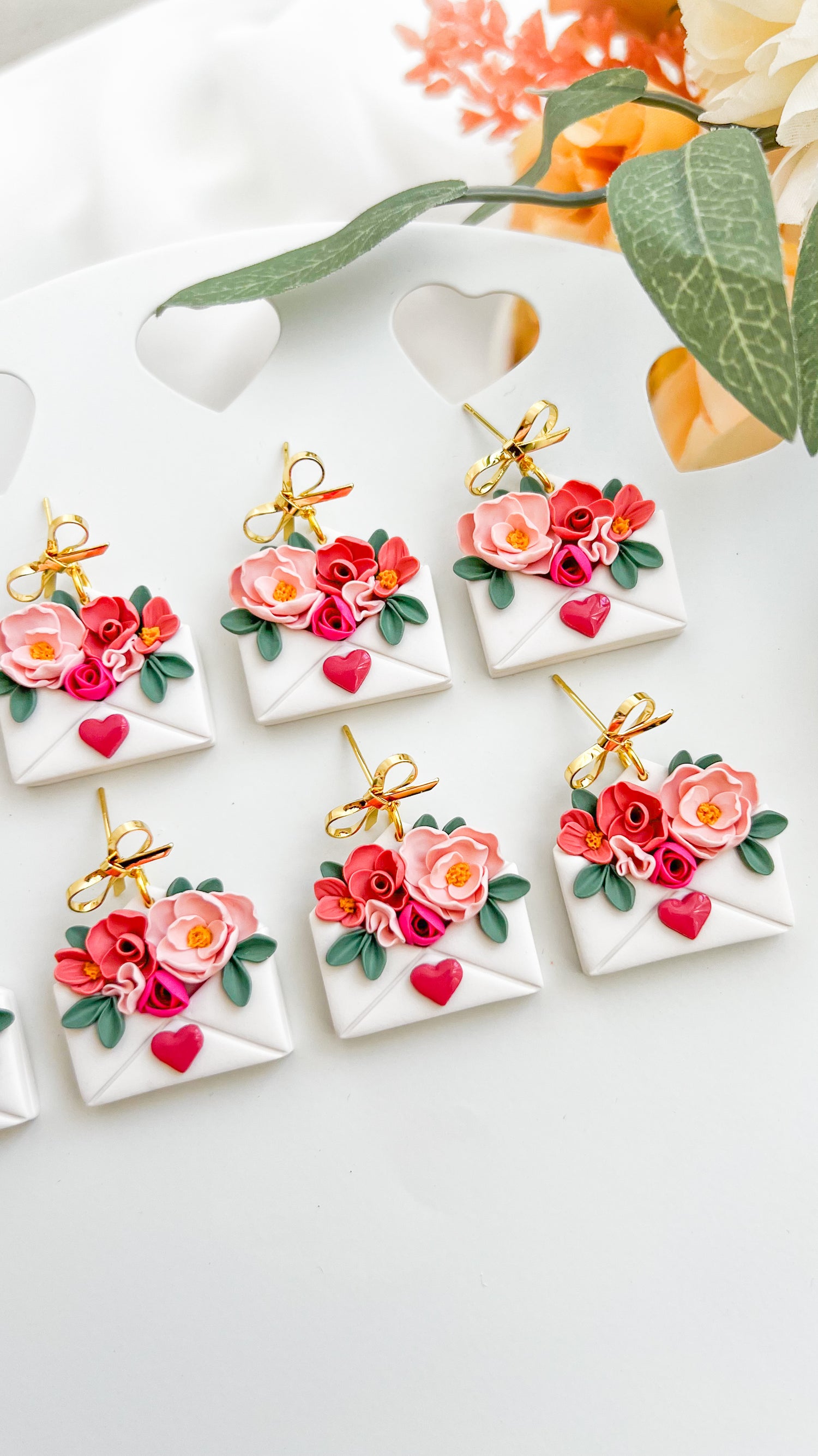 Decorative envelope earrings with floral designs and small bows on a white surface.