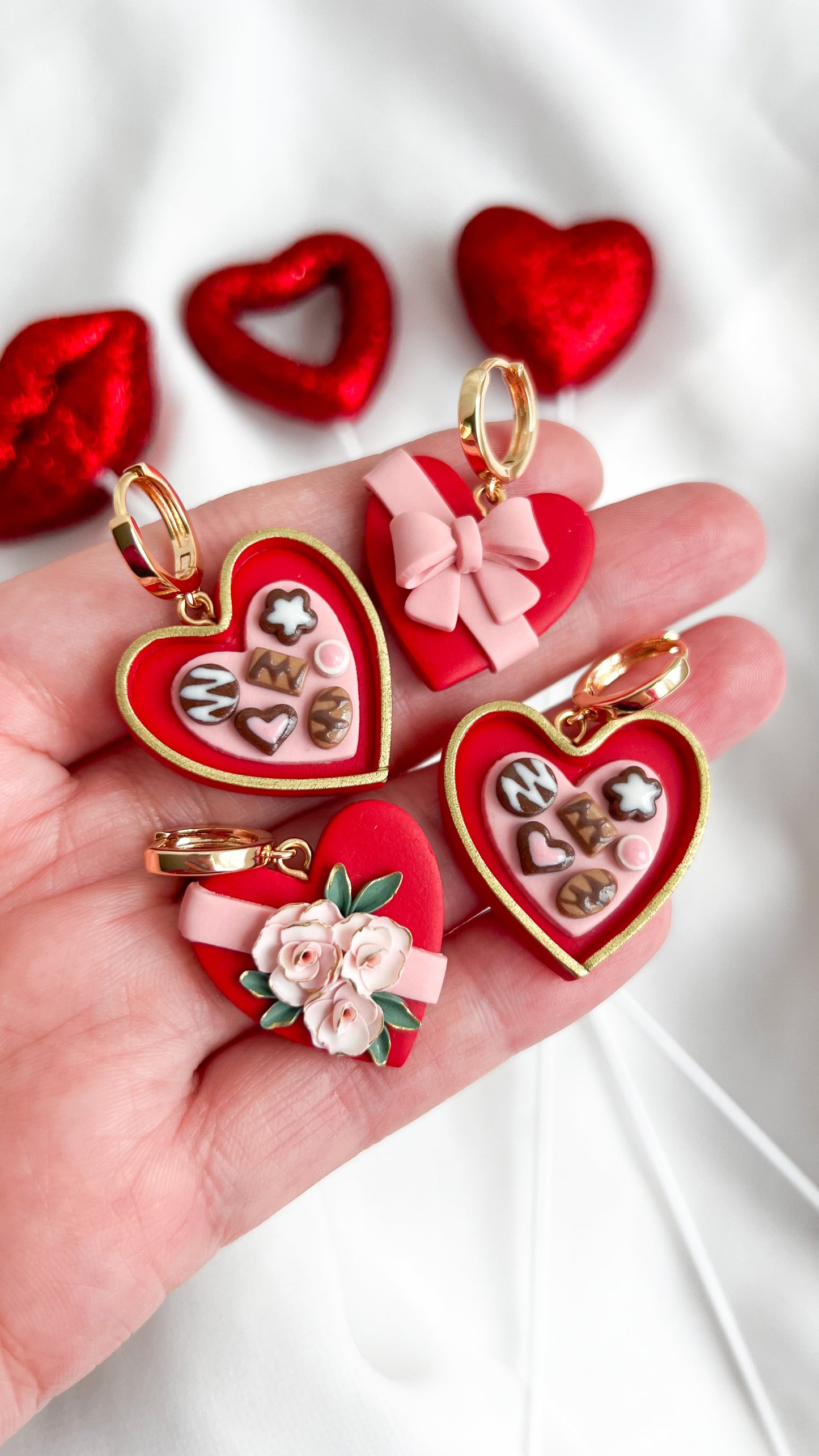 Heart-shaped chocolate heart box earrings with decorative elements held in a hand against a white background