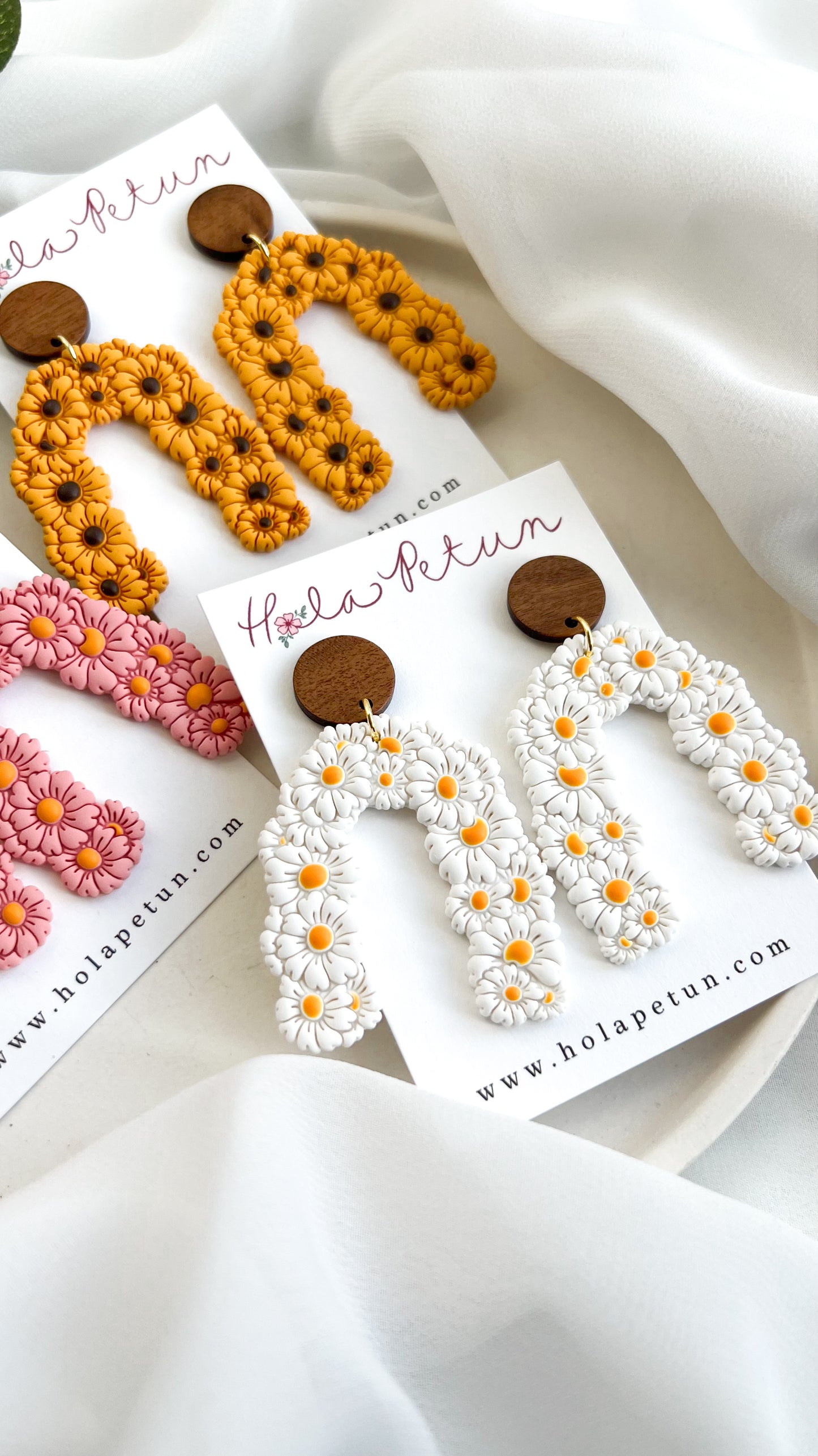 Three pairs of earrings on cards with 'hola petun' branding, featuring floral designs.