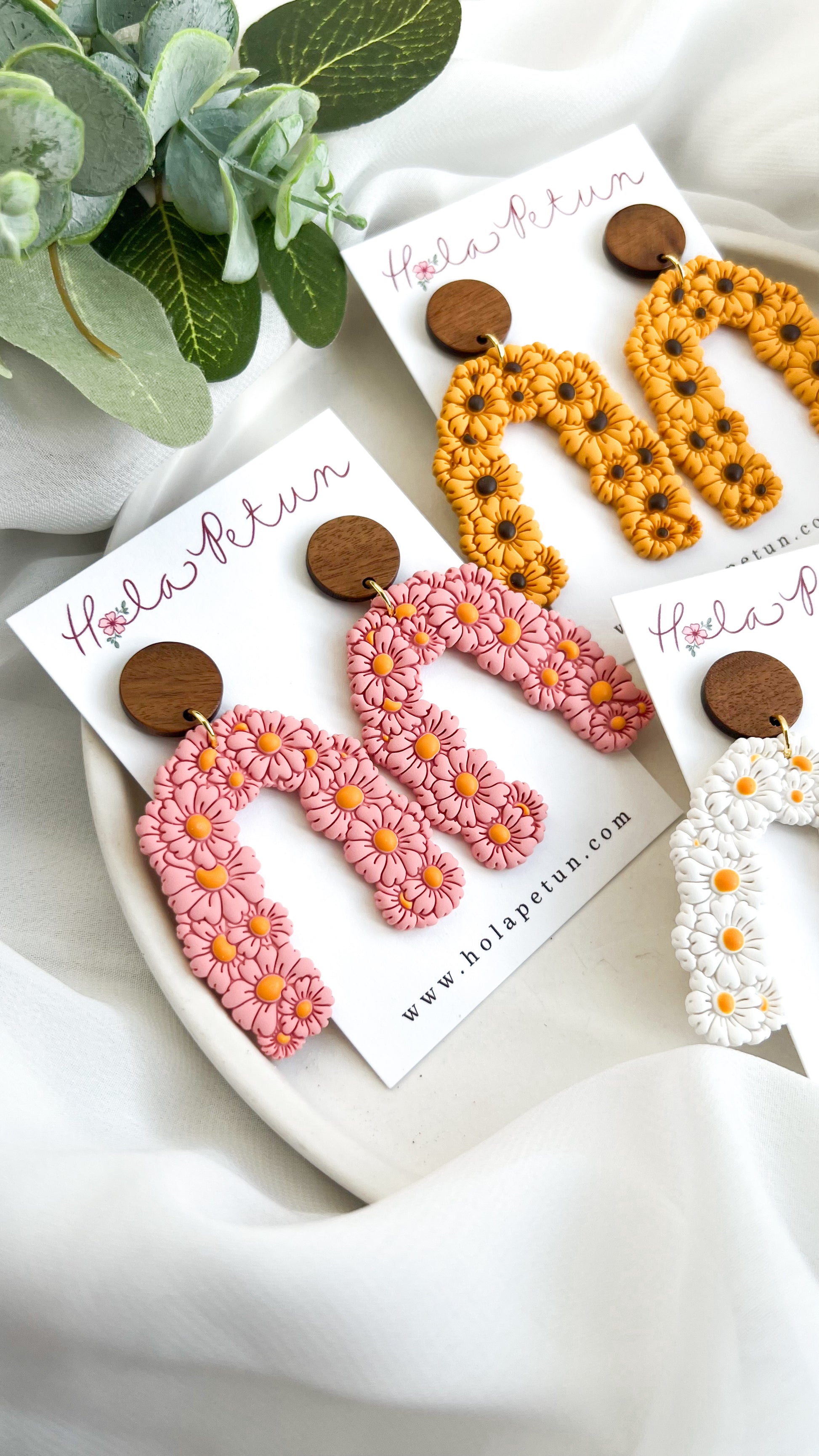 Pair of floral earrings on branded card with a plant in the background