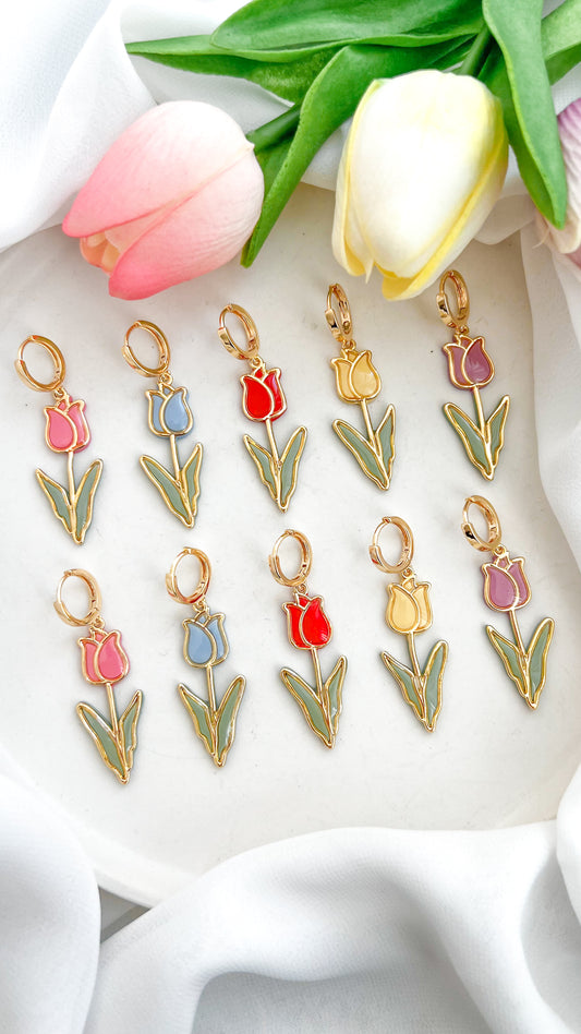 Set of tulip-shaped polymer clay earrings in various colors, pink, blue, red, yellow and purple on a white fabric background with tulips.